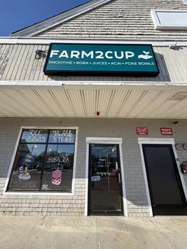 Farm2Cup cafe exterior featuring the sign with offerings of smoothies, boba, juices, acai, and poke bowls, located in Fairhaven, emphasizing healthy eating and community focus.